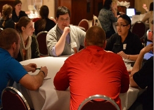 Students, GVSU alumni sitting at a table and participating in an activity (photo).